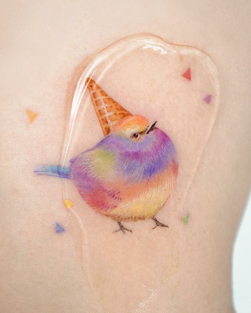Colorful painting-like tattoo of a bird with an ice cream cone hat on skin.