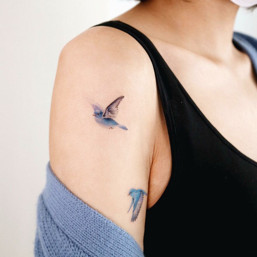 Painting-like tattoos featuring delicate blue birds on a person's arm.
