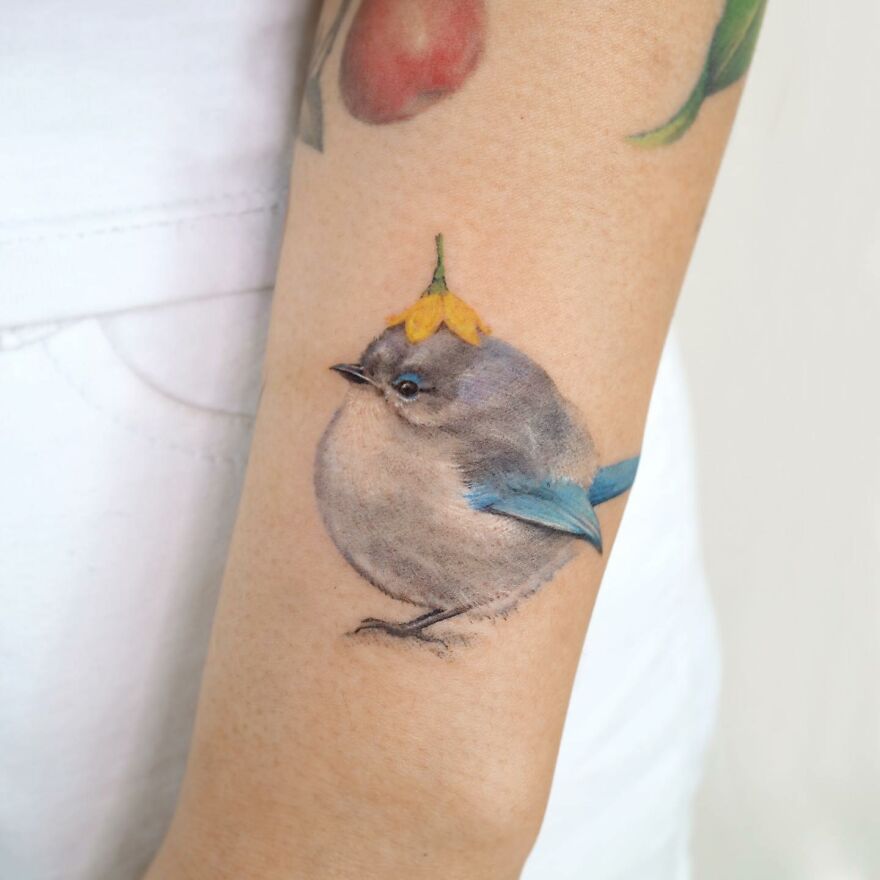 A bird tattoo on an arm, featuring painting-like details and vibrant colors, resembling art by the artist.