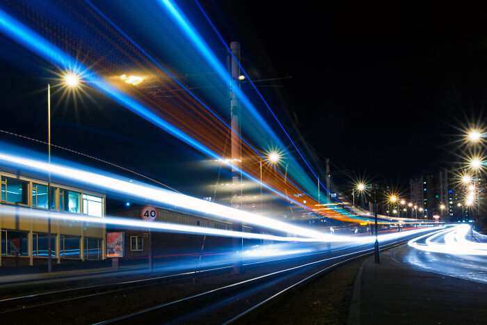 Long exposure photo of a tram at night, creating ethereal light trails on city tracks.