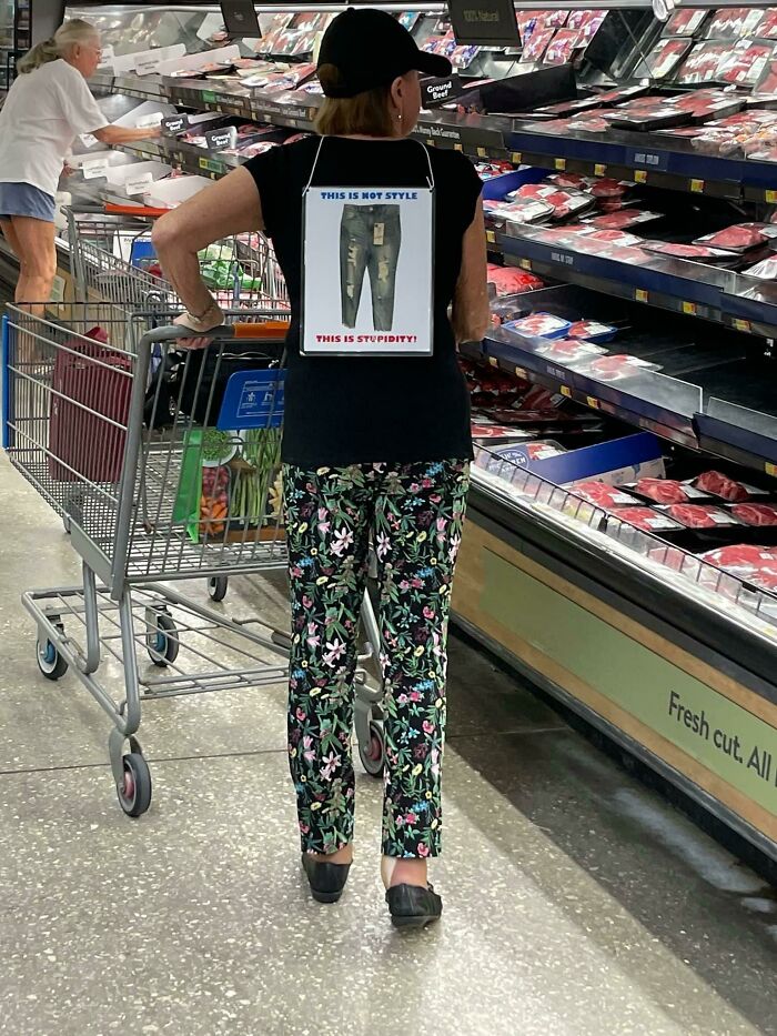 Woman with a cart in a meat isle with a funny poster on her back 