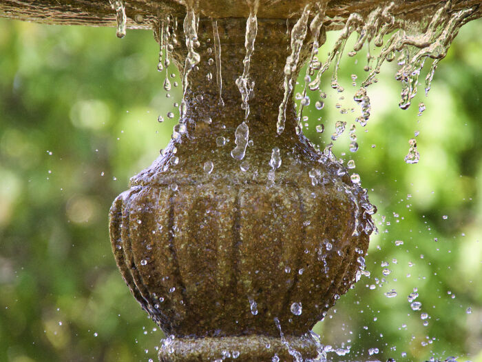 Nature photo of water droplets cascading from a stone fountain, capturing light and motion in a vibrant outdoor setting