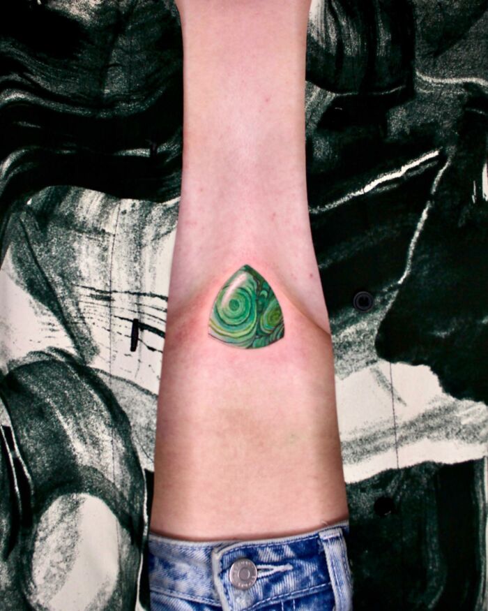 Forearm displaying a green geometric tattoo, known as "permanent jewelry," showcasing intricate patterns.