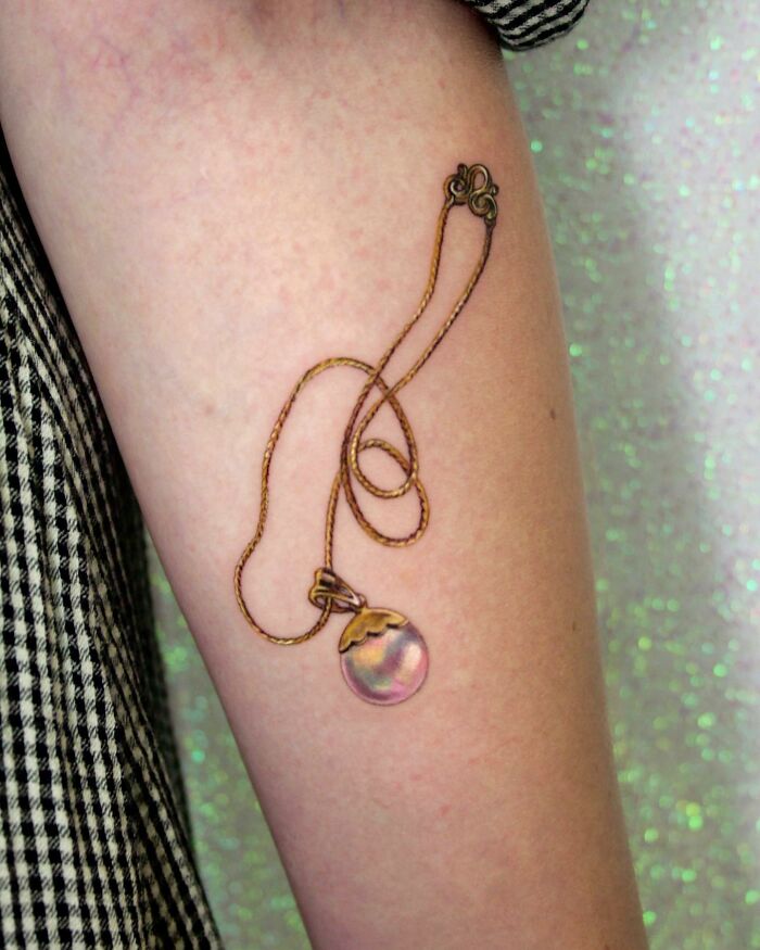 "Permanent jewelry tattoo on arm displaying intricate necklace design."