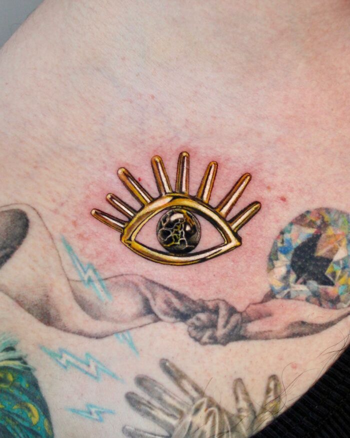Eye tattoo with golden lashes and marble center, symbolizing permanent jewelry on skin.