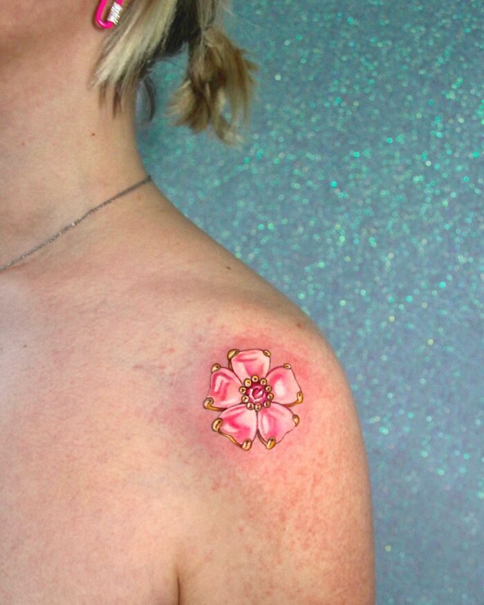 Pink flower tattoo on shoulder showcasing permanent jewelry design.