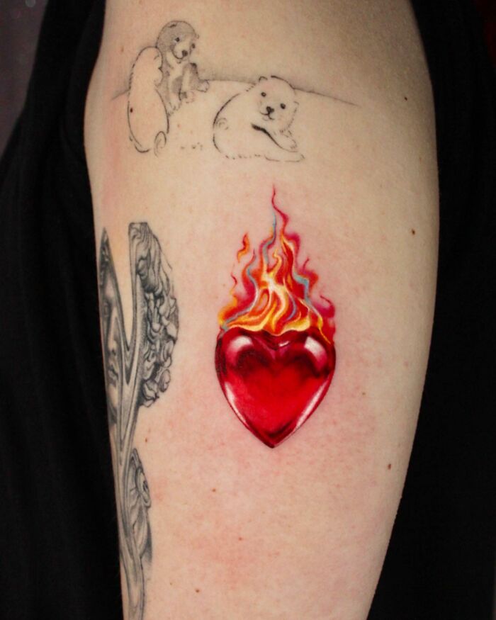 Tattooed arm featuring vibrant heart with flames and bear sketches, showcasing permanent jewelry-inspired tattoos.