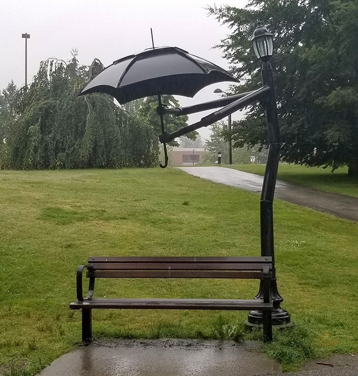 Este poste de luz sostiene un paraguas sobre el banco