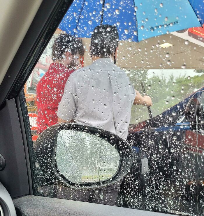 El gerente sujeta el paraguas a un empleado que está cambiando las escobillas del limpiaparabrisas mientras llueve