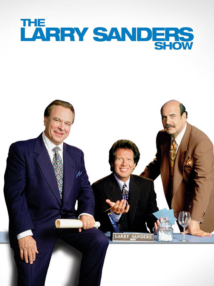 Cast of "The Larry Sanders Show," a highly acclaimed HBO TV show with three men smiling at a desk.