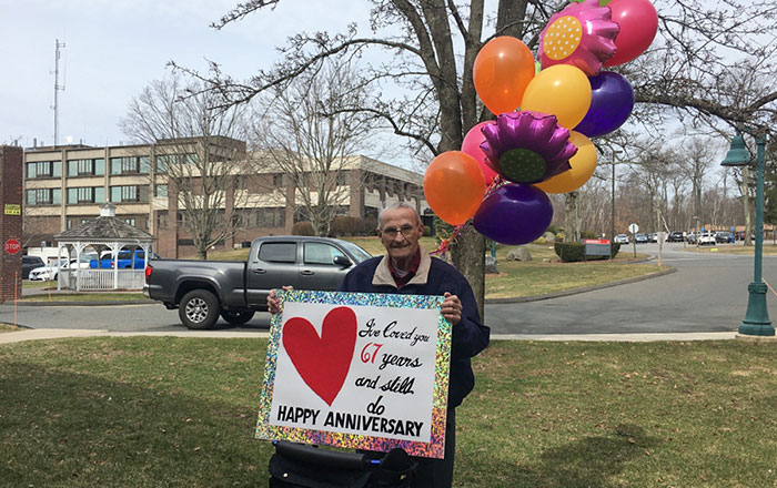 El marido sostiene una pancarta para su mujer fuera de la residencia de ancianos en su 67º aniversario después de que le prohibieran las visitas