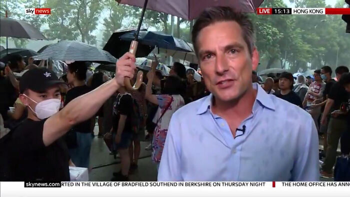 Protestor Hold Umbrella Over Journalist