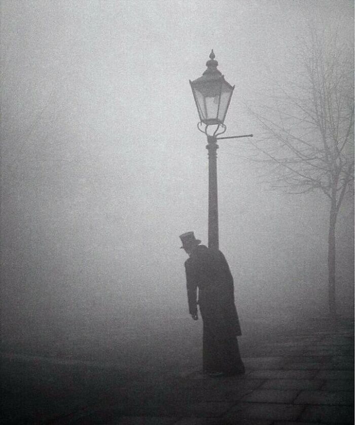 A Drunken Man In Top Hat And Tails Clings To A Lamp-Post In Early Morning Fog, London. This 1934 Photo Was By Acclaimed Photographer, Bill Brandt.