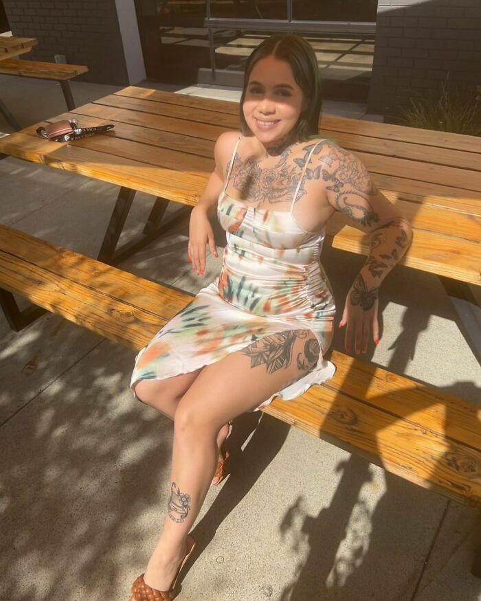 Woman with tattoos sitting on a bench in sunlight, wearing a colorful dress. Woman with tattoos sitting on a bench in sunlight, wearing a colorful dress.