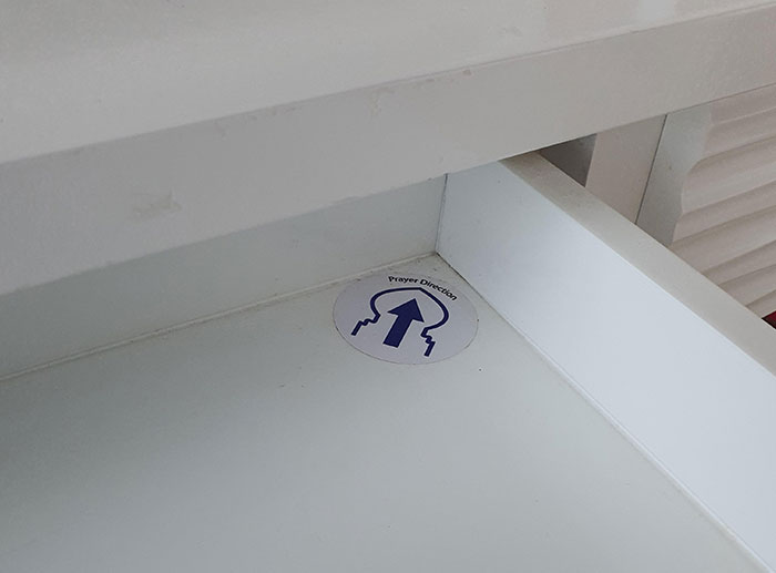 The Drawer In My Hotel Room Has A Sticker Pointing To "Prayer Directions"