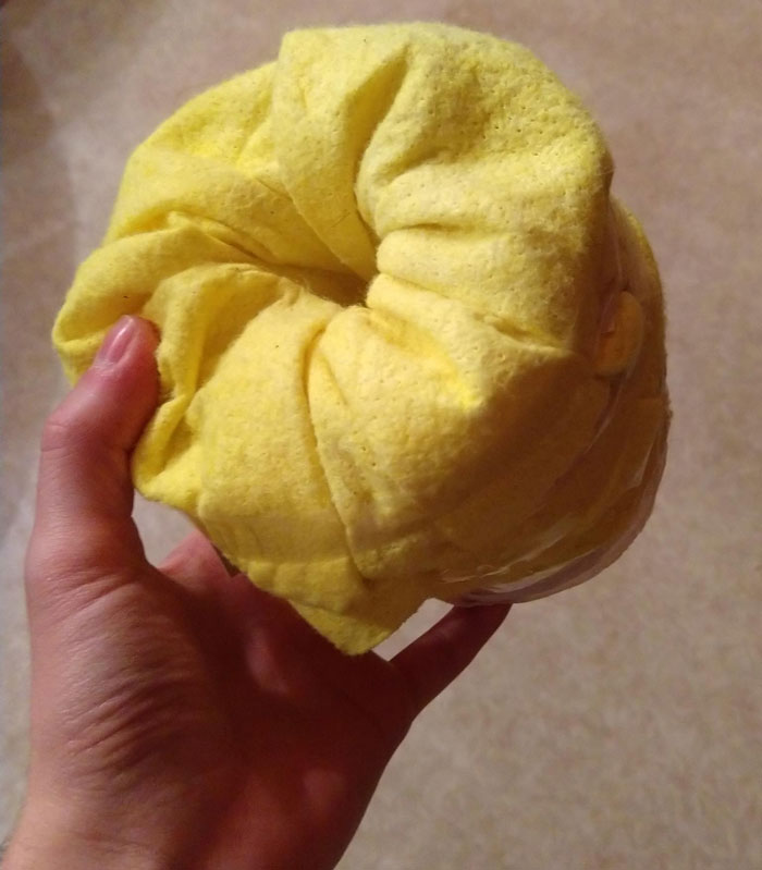 It's A Toilet Paper Roll Wrapped In A Yellow Cleaning Cloth, That Is Attached By Gummy Strings And Clear Tape. The Cloth Is Stuffed Into The Roll On One End