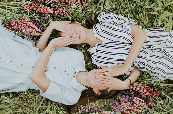 Two woman laying on grass covering each others hands 