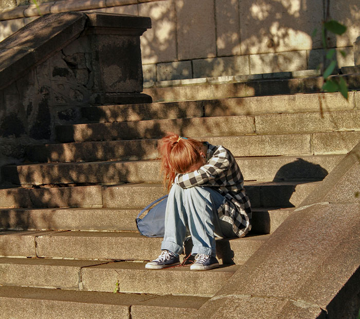 Sad ginger girl sitting on stairs with her head down 