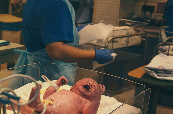 Crying baby in an incubator with nurse nearby 