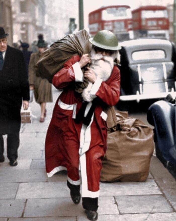 Father Christmas Wearing A Tin Helmet Walking On Regent Street In London, England Carrying A Bag Of Presents. Photograph Taken On The 23 December 1940