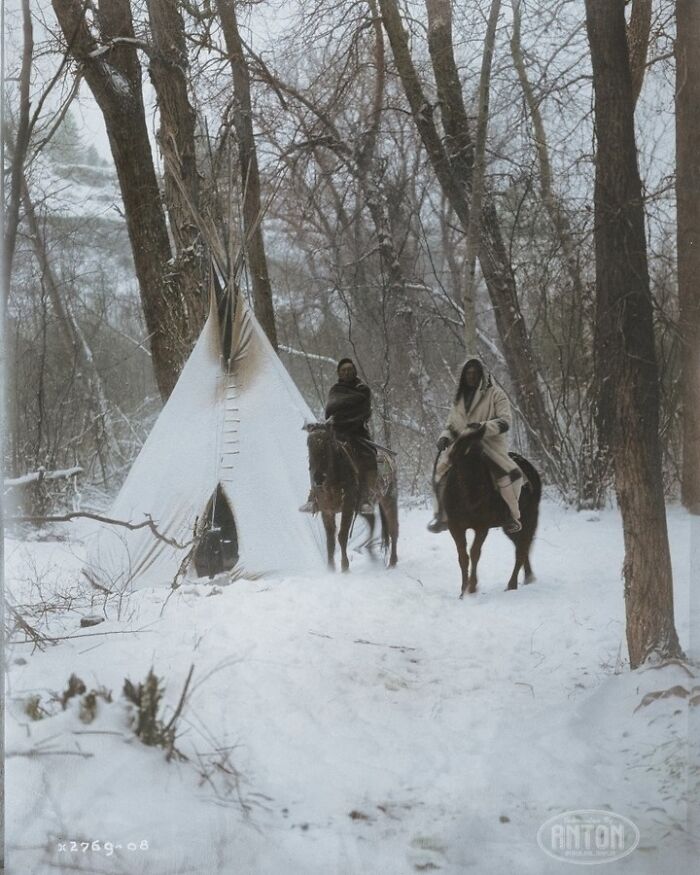 Los nativos americanos Wo Apsaroke a caballo fuera de un tipi en un bosque cubierto de nieve en Montana en 1908