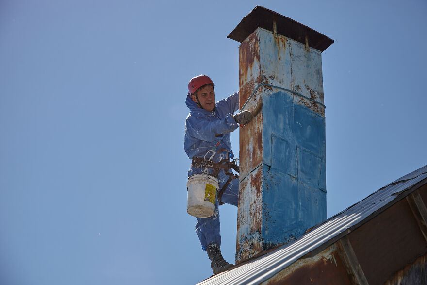 The Painter-Climber Paints The Chimney. A Worker On A Blue Sky Background.