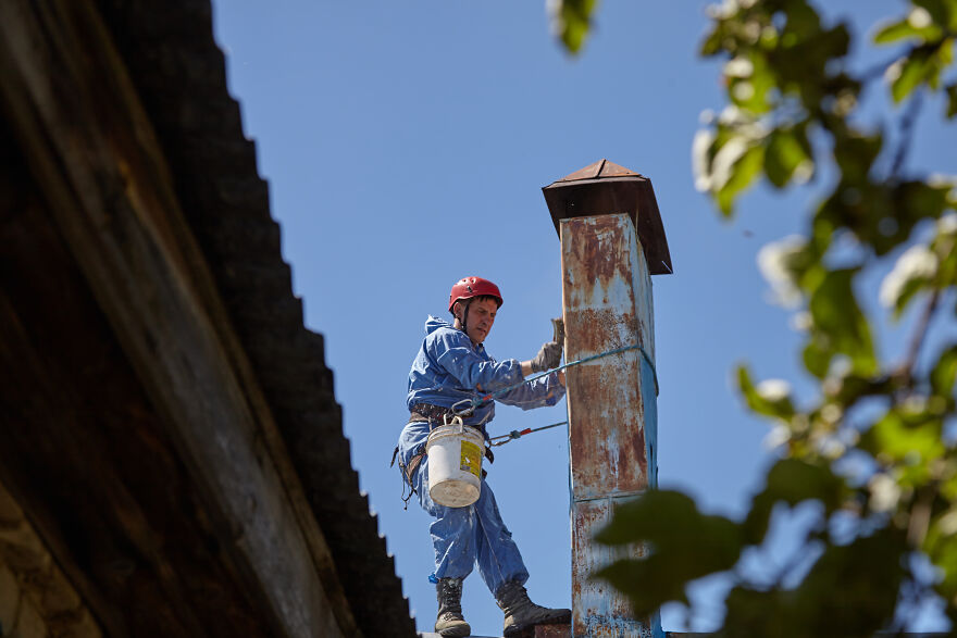The Painter-Climber Paints The Chimney. A Worker On A Blue Sky Background.