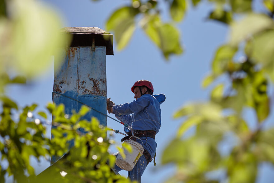 The Painter-Climber Paints The Chimney. A Worker On A Blue Sky Background.