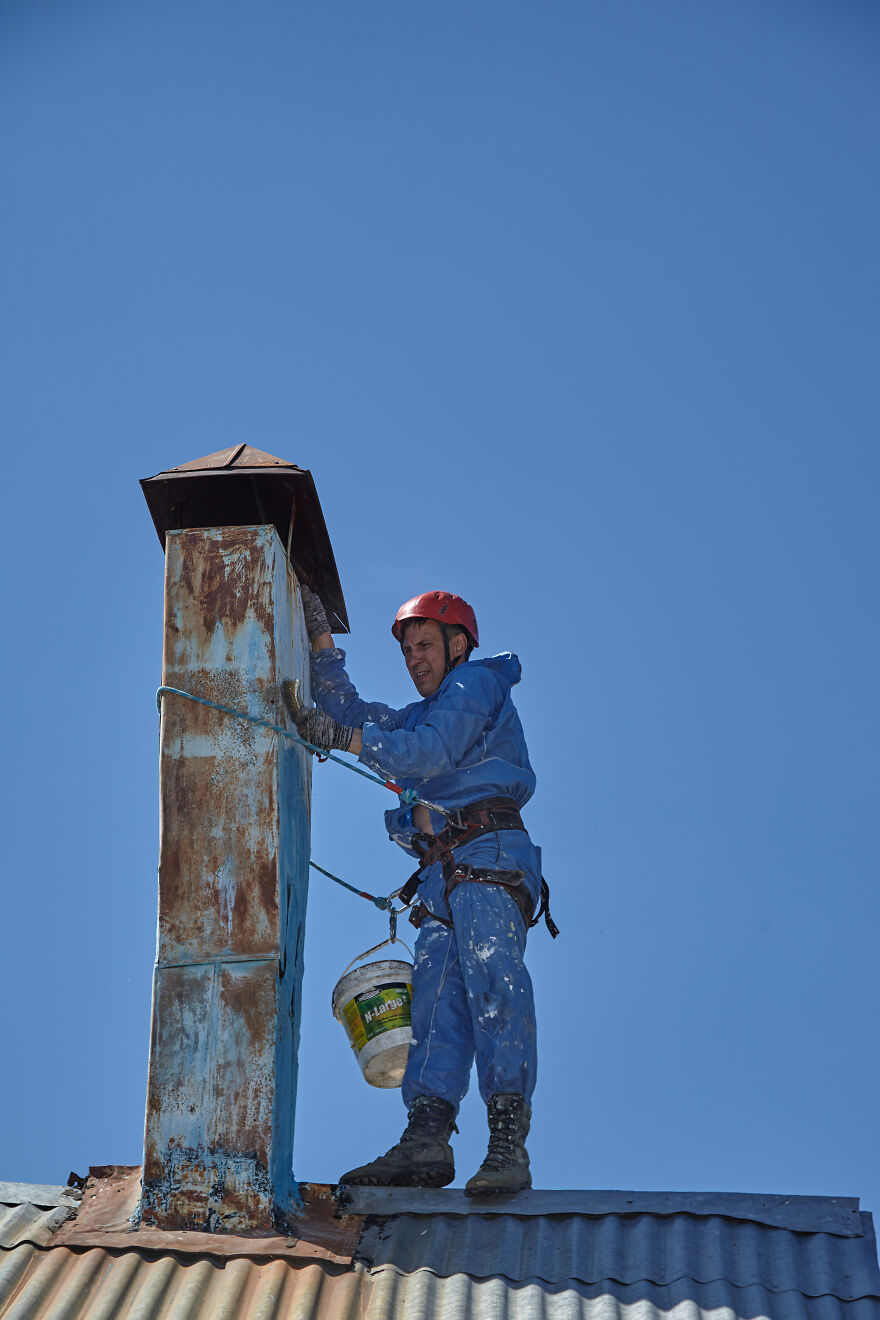 The Painter-Climber Paints The Chimney. A Worker On A Blue Sky Background.