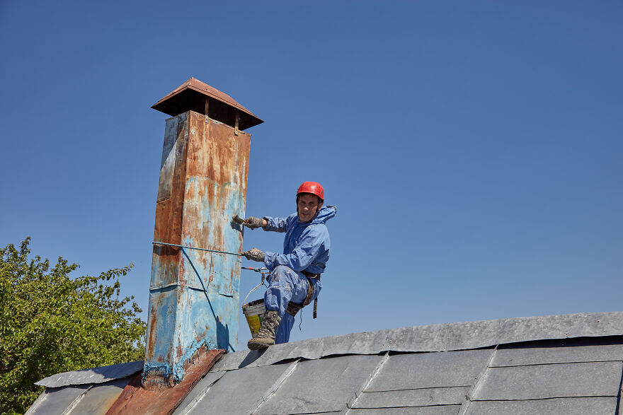 The Painter-Climber Paints The Chimney. A Worker On A Blue Sky Background.