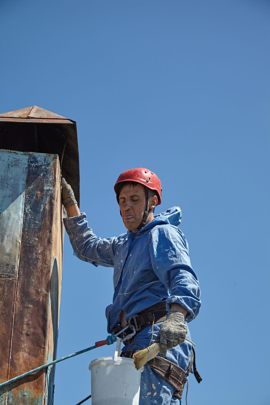 The Painter-Climber Paints The Chimney. A Worker On A Blue Sky Background.