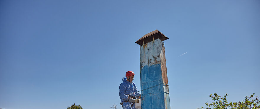 The Painter-Climber Paints The Chimney. A Worker On A Blue Sky Background.