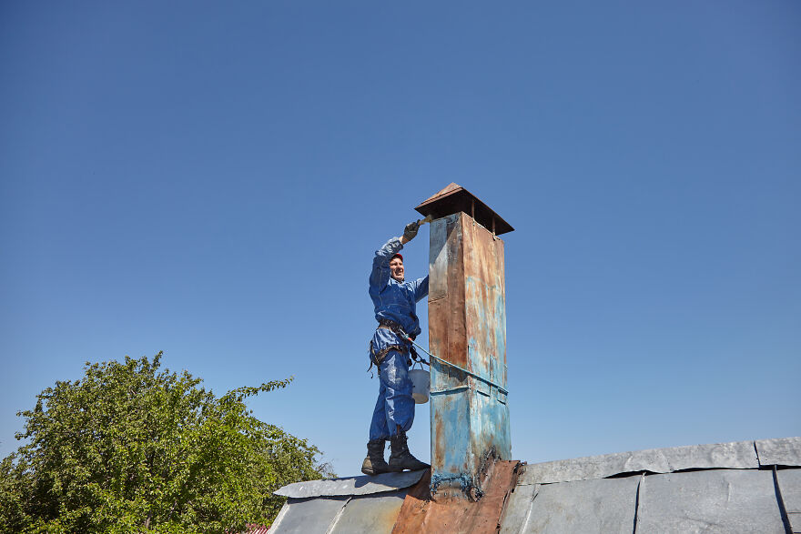 The Painter-Climber Paints The Chimney. A Worker On A Blue Sky Background.