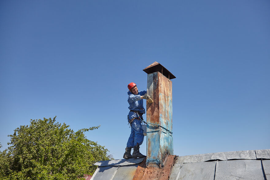 The Painter-Climber Paints The Chimney. A Worker On A Blue Sky Background.