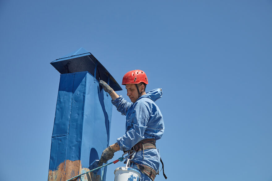 The Painter-Climber Paints The Chimney. A Worker On A Blue Sky Background.