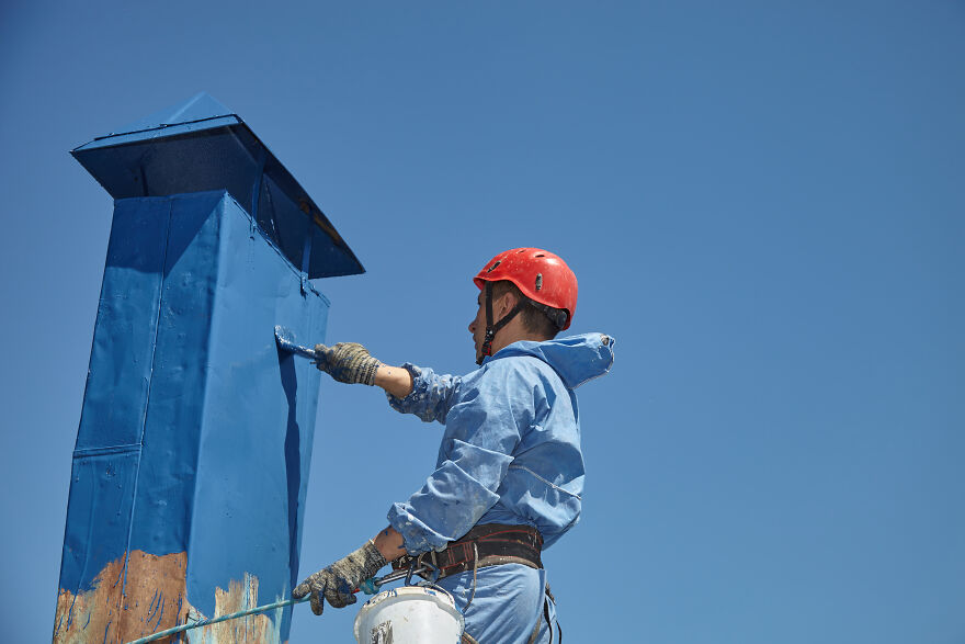 The Painter-Climber Paints The Chimney. A Worker On A Blue Sky Background.
