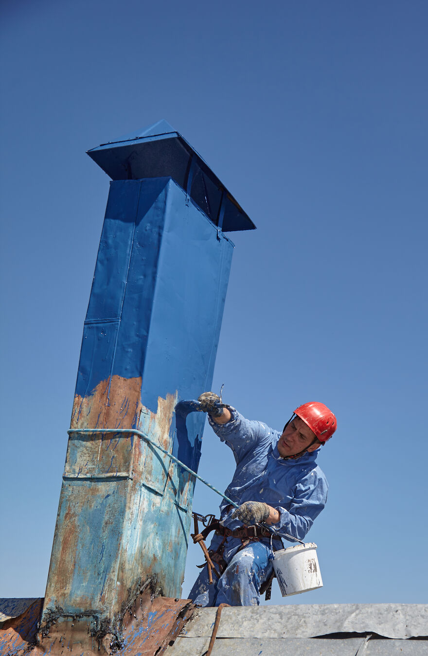 The Painter-Climber Paints The Chimney. A Worker On A Blue Sky Background.