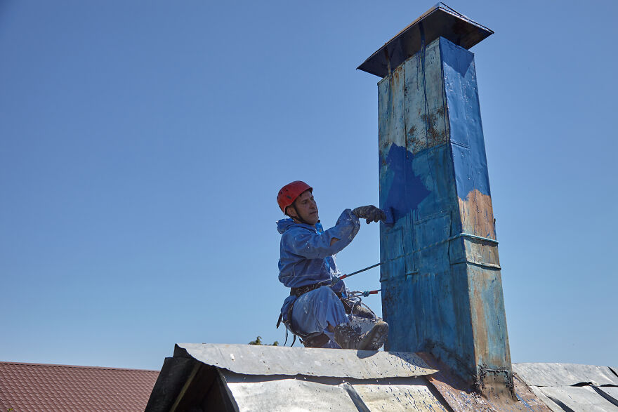 The Painter-Climber Paints The Chimney. A Worker On A Blue Sky Background.
