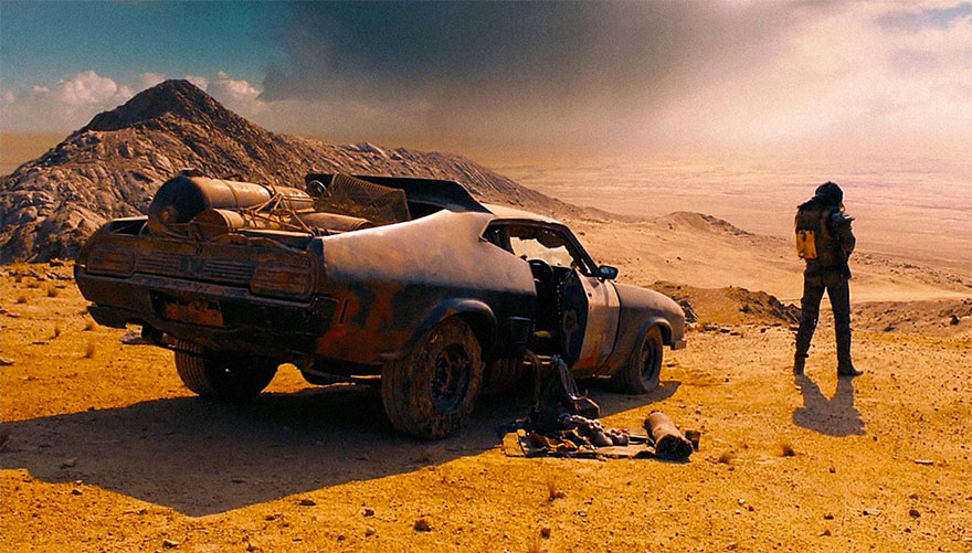 A man stands near a vehicle in a desert