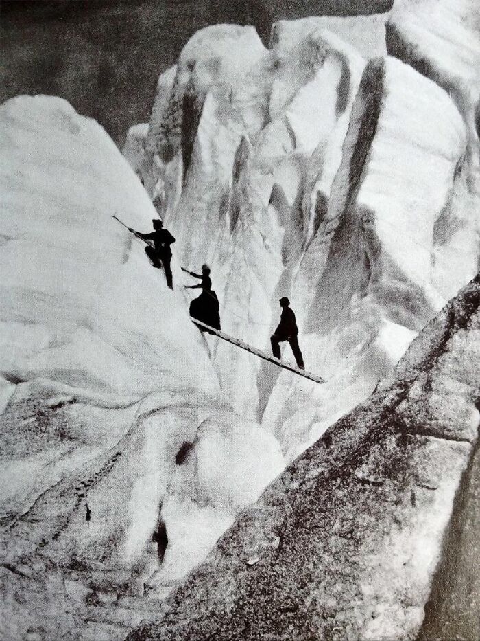 Montañeros de finales de la época victoriana, incluida una dama completamente vestida y con corsé, cruzan una grieta en los Alpes (1900)
