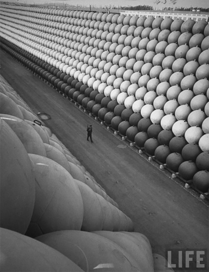 A Security Guard Walking Down Us Highway 101 Where There Are Towering Stacks Of Hollow Iron Floats From Which The Iron Antisubmarine Nets Were Suspended To Protect The Us Ports During The Last War, By Hank Walker, 1953