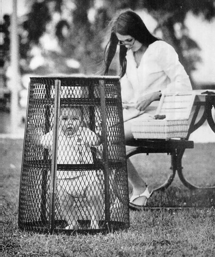 Una madre utiliza un cubo de basura para contener a su bebé mientras hace ganchillo en el parque, 1969