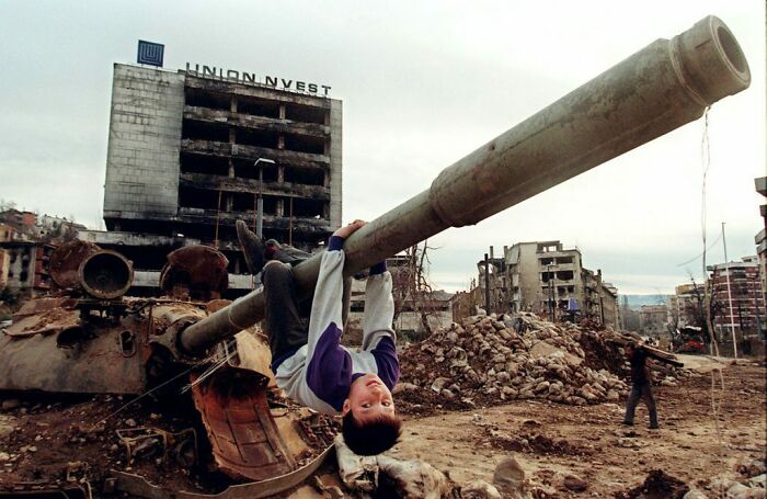 Young Boy In Sarajevo Using A Destroyed Tank's Cannon As Makeshift Monkey Bars To Have Some Fun, During The Bosnian War (1990s)