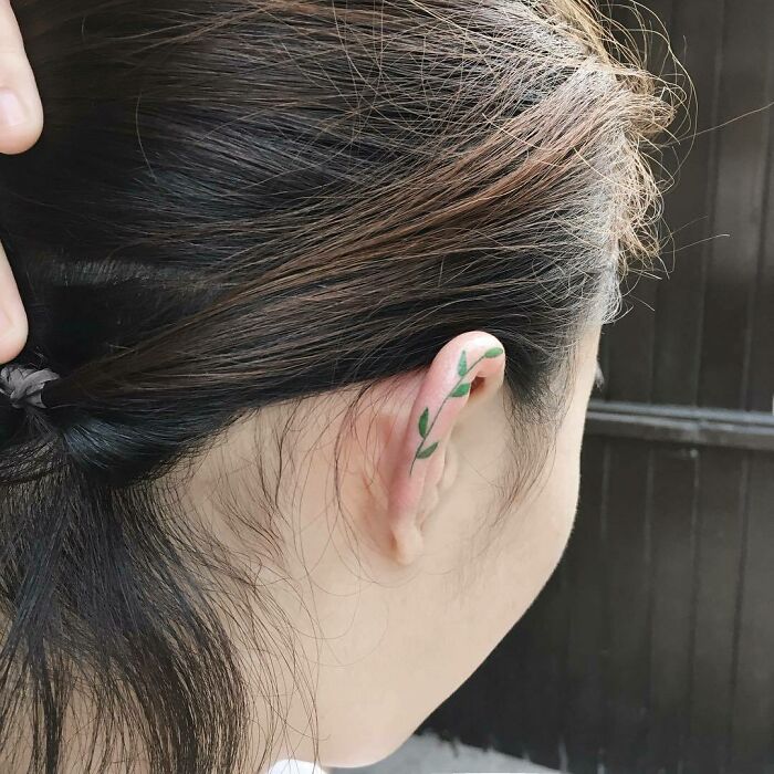 Woman with a subtle leaf ear tattoo, hair pulled back to reveal the design.