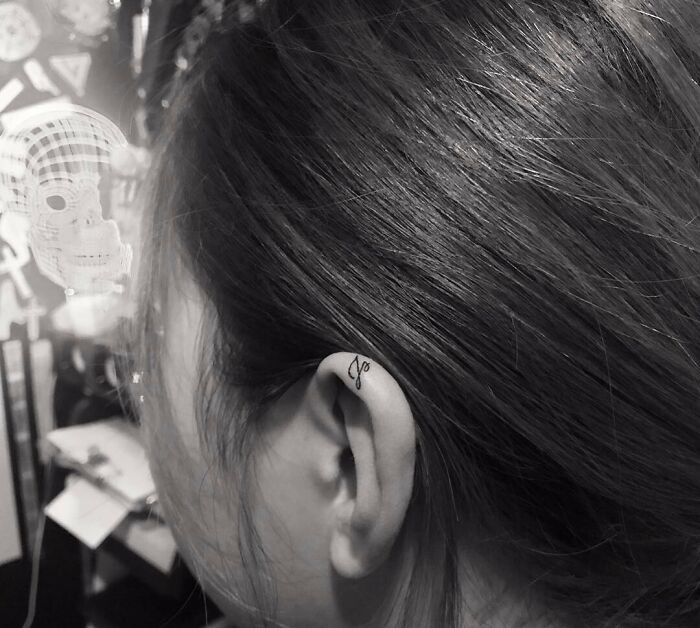 Minimalist ear tattoo with delicate script on the ear's edge, showcasing subtle artistry and unique style.