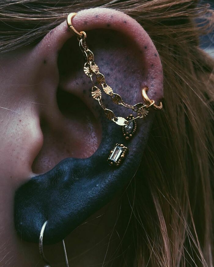 Ear with black tattoo ink and gold piercings, showcasing a unique ear tattoo style.