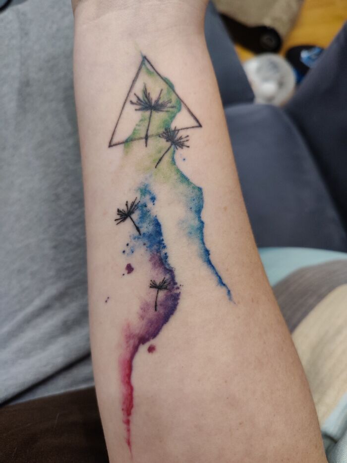 Close-up of a colorful watercolor tattoo with dandelions on an arm, featuring triangle design elements.