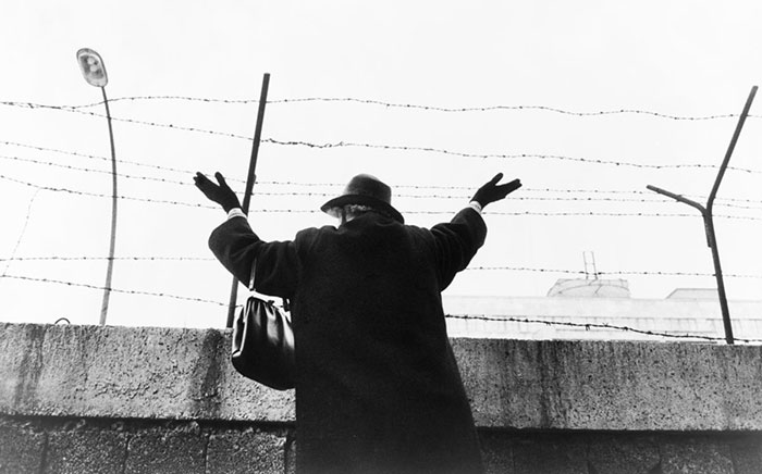 Vista trasera de una mujer de pie junto al muro de Berlín, en el sector occidental, con las manos levantadas. Después de esperar tres horas para ver a sus amigos y familiares de Berlín Oriental