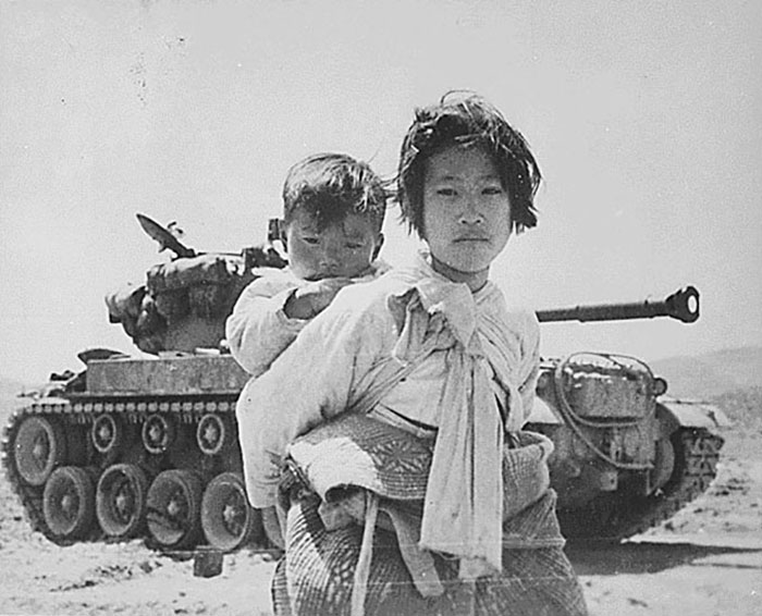 Con su hermano a la espalda, una niña coreana cansada de la guerra pasa junto a un tanque M-26 detenido en Haengju, Corea. 06-09-1951