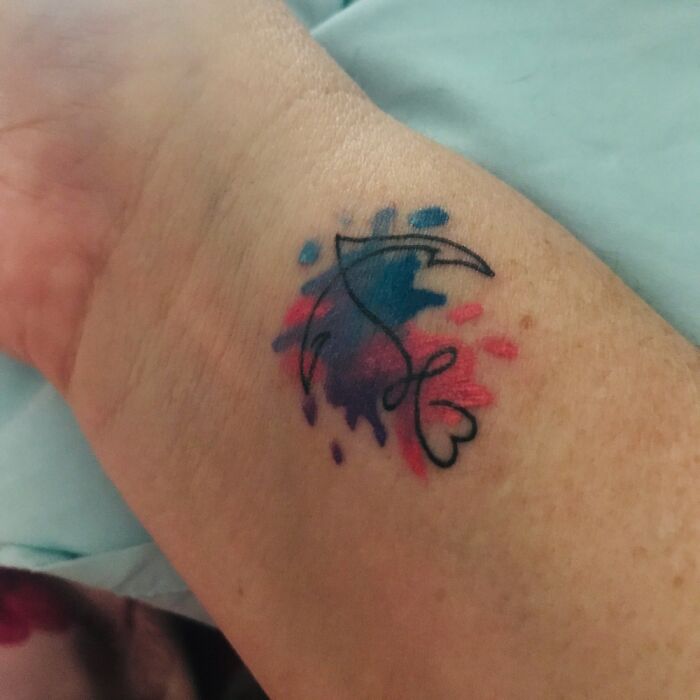 Colorful abstract tattoo on an arm featuring a black-line design with blue and pink watercolor splashes.